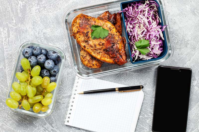 fruit and protein around a notepad and phone for meal planning.